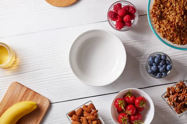 sağlıklı bir kahvaltı için-malzemeler granola, fındık, ahududu, çilek, yaban mersini kase Beyaz ahşap zemin üzerinde. Üstten görünüm, kopya alanı