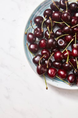 Organik taze kiraz bir gri taş zemin üzerine mavi bir seramik tabak içinde metin için yer. Üstten görünüm.