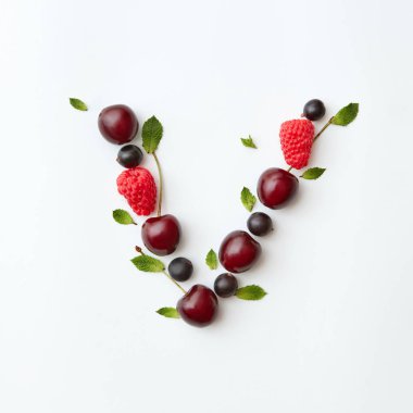 Mektup V alfabe yapılan doğal organik çilek, Olgun taze ahududu, siyah frenk üzümü, kiraz İngilizce, beyaz zemin üzerine yeşil nane yaprakları