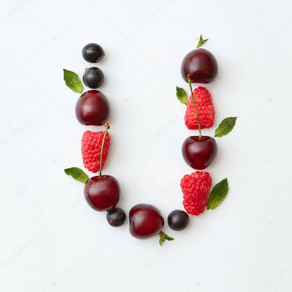Letter U of English alphabet made of natural organic berries, ripe fresh raspberries, black currant, cherries, green mint leaves on white background
