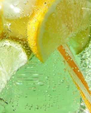 Bir bardak limonata buzlu canlandırıcı bir soğuk ile bir makro çekim, kireç, limon ve nane yaprakları, yeşil bir arka plan üzerinde plastik çöp. Bir cam kavanoz içinde hava kabarcıkları.