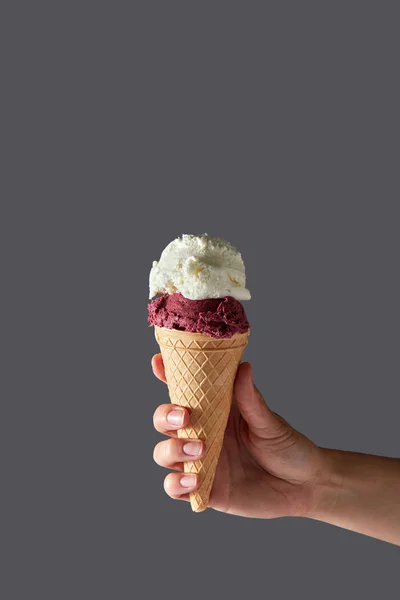一只女性手在灰色背景的华夫饼圆锥中拿着红莓冰淇淋和白牛奶冰淇淋 带有复制空间的夏季概念 — 图库照片