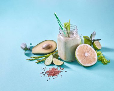yeşil smoothie ve taze sebze ve meyve, kireç, avokado, salatalık, kuşkonmaz ve mavi arka plan üzerinde keten tohumu ile jar 