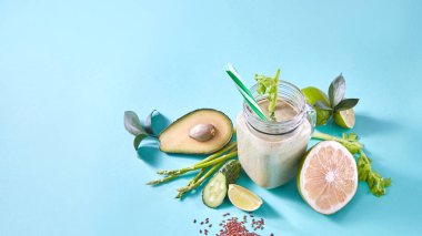 yeşil smoothie ve taze sebze ve meyve, kireç, avokado, salatalık, kuşkonmaz ve mavi arka plan üzerinde keten tohumu ile jar 