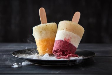 Ev yapımı meyve bir çubuk siyah bir plaka üzerinde lolly sorbe koyu ahşap bir masa üzerinde eriyen buz parçaları ile dut. Sağlıklı tatlı soğutma