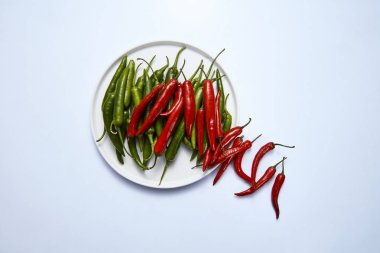 Kırmızı ve yeşil biber izole beyaz bir arka plan üzerinde beyaz bir plaka üzerinde bir bileşimi. Üstten görünüm.