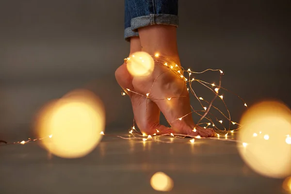 床の上のクリスマスの花輪が飾られて暗い背景黄色のライトのぼかしと周りの女性の足 コピー スペース — ストック写真