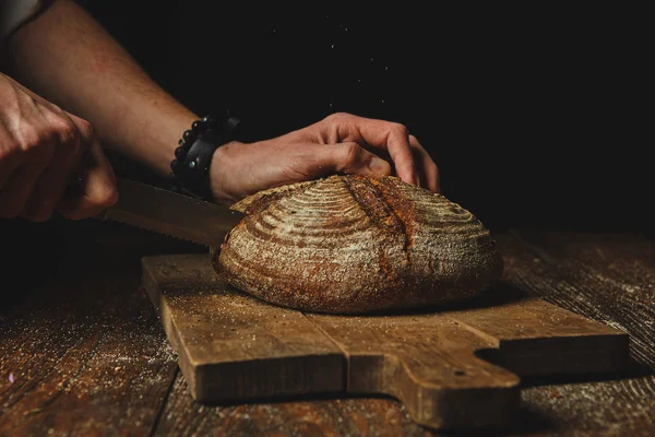 Rukou Mladého Muže Snížit Čerstvý Žitný Chléb Dřevěné Prkénko Tmavém — Stock fotografie