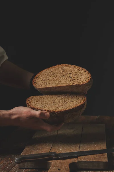 Человек Пекарь Держит Руках Половинки Ржаного Хлеба Фоне Старого Коричневого — стоковое фото