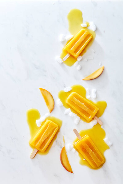 Food pattern from splashes of melting fruit ice cream on a stick of ice and peach slices on a gray marble background with copy space. Layout for your ideas. Flat lay