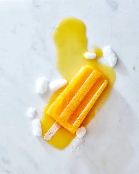 Composition of pieces ice and melting ice cream on a stick with splashes on a gray marble table with copy space. Layout for your ideas. Flat lay