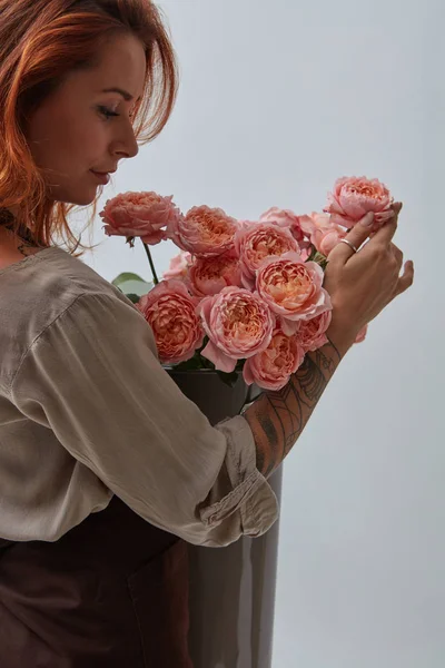 性感的红头发女孩与纹身 持有一个美丽的花束粉红色玫瑰在一个花瓶周围的灰色背景与复制空间 明信片到情人节 — 图库照片