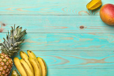 Tropikal meyve, muz, mango, carambola ve ananas kopya alanı bir mavi ahşap zemin üzerine köşe çerçevelemek. Düz yatıyordu