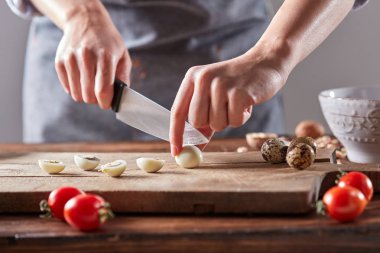 Ahşap bir masa üzerinde bir kadın elinde Bıldırcın yumurta eski ahşap panosunda kesti. Adım adım salata hazırlık tarafından