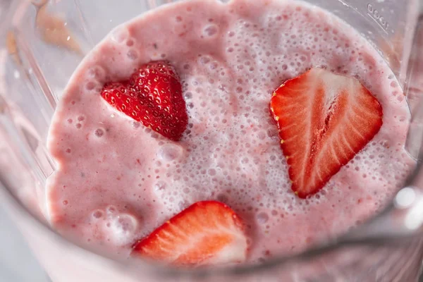 牛奶饮料与健康的草莓片在搅拌机特写镜头 自制的浆果奶昔 顶视图 — 图库照片