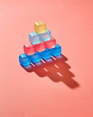 2019 yaşayan mercan Pantone yılın bir renkte bir arka plan üzerinde renkli plastik buz küpleri ile zor geometrik piramit gölgeler. Metin için yer.