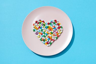 Birçok farklı hapları ve mavi bir arka plan üzerinde beyaz bir plaka üzerinde bir kalp şeklinde takviyeleri. Kardiyovasküler hastalıkların önlenmesi. Düz yatıyordu