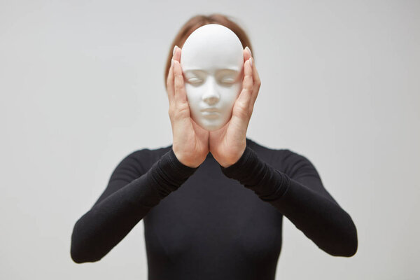 Attractive girl in a black sweater holding gypsum sculpture mask instead of face on a white background, place for text. Concept The masks we wear.