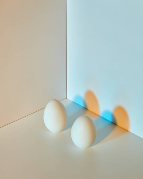 Два яйца на двойном серо-голубом фоне с отражением оранжево-голубых теней и пространством для текста. Пасха
.