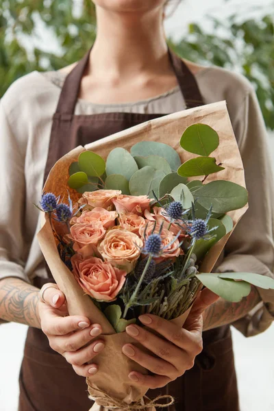 Florist woman with a bouquet of coral roses and green leaf. Girl is holding a flowers in her hands. The gift to Mother\'s Day.