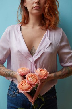 Pembe güller bir buket kopya alanı ile mavi bir arka plan etrafında dövme seksi bir kızıl saçlı kız elinde tutuyor. Sevgililer günü konsepti