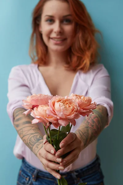 一个快乐的红头发的女人 有纹身 手里拿着精致的粉色玫瑰 蓝色的背景和文字的复制空间 节日礼品概念 — 图库照片