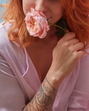 Fresh fragrant living coral colored rose in a girl's hands with tattoo. Smiling young pretty woman with ginger hair. Creeting card of Woman's or Mother's Day. Close-up. clipart