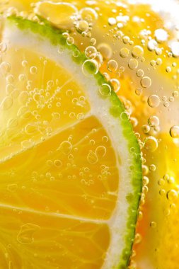 Su ile bir bardak kabarcıklar çok sarı limon dilimleri ve kireç Makro fotoğraf. Yaz ferahlatıcı kokteyl