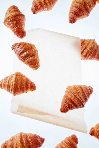 Fliegende Französische Croissants Und Ein Stück Backpapier Auf Hellem Hintergrund — Stockfoto