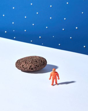 Mavi yıldızlı gökyüzü arka plan karşı taş ve gölgeler ile hafif bir zemin üzerinde Oyuncak plastik astronot. Metin için yer. Dış uzay kavramı.