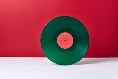 Bir duotone kırmızı gri arka plan üzerinde yuvarlak müzik yeşil vinil kayıt. Retro ses teknolojisi. Metin için yer.