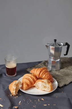Gri bir arka plan üzerinde taze pişmiş Fransız kruvasan ile aromatik sıcak kahve ve tabak cam. Kontinental kahvaltı konsepti. Metin için yer.