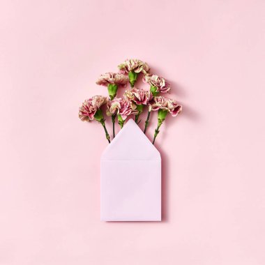 Kopya alanı ile açık pembe bir arka plan üzerinde el yapımı boş bir zarf içinde taze karanfil Buket. Mock. Üstte görüntü.