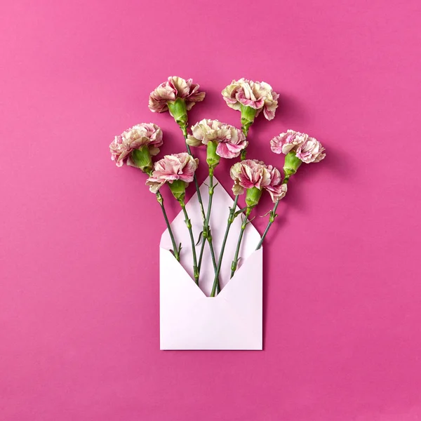 マゼンタの背景にカーネーションの花と手工芸品の空白の封筒 コピースペース トップビュー グリーティング カード — ストック写真