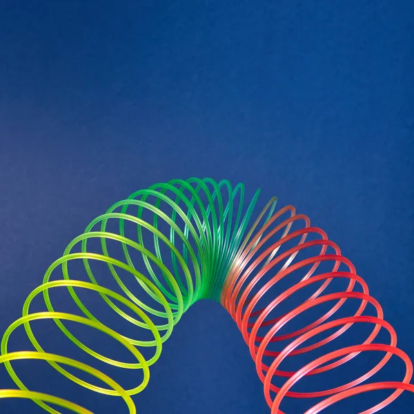 柔性彩虹塑料弹簧 在蓝色背景上以抛物线的形式出现 带有文本位置 — 图库照片