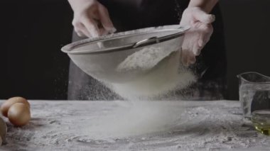 Kadın elleri unu süzgeçten geçirir, hamur yoğurur.