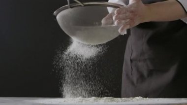 Kadın elleri unu süzgeçten geçirir, hamur yoğurur.