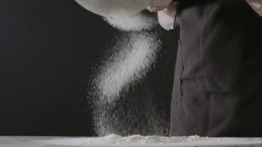 Kadın elleri unu süzgeçten geçirir, hamur yoğurur.