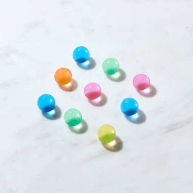 İçinde kristal renkli Iquid bulunan hidrojel topları, sert gölgeler ve yansımalarla dolu gri mermer bir masanın köşegen desenleri, kopyalama alanı. Üst görünüm.