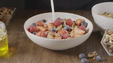 Doğal organik süt ya da yoğurdu sağlıklı granola ve taze organik meyve ve böğürtlen ile seramik kaseye dökme videosu. Ağır çekim, 2K video, 240 fps, 1080p.