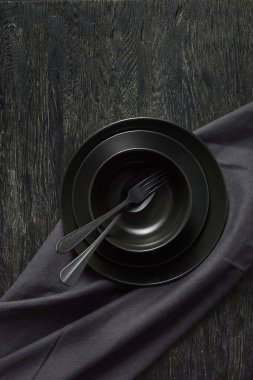 Farklı seramik tabaklardan akşam yemeği. Kaşık, çatal, tekstil havlusu ya da peçeteyle servis edilen siyah renkler. Aynı renk taş arka planda, kopyalama alanı. Üst görünüm.