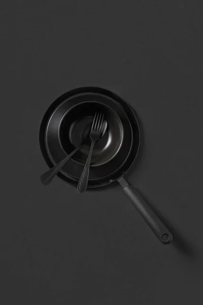 黒い色のキッチン用品から設定されたディナーテーブル 同じ色の背景にフォークとスプーンで空のプレートとパン コピースペース トップ表示 — ストック写真