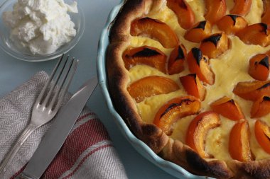 Krem şanti, çatal ve bıçak ve keten mutfak havlusu, yüksek açılı görünüş, yakın çekim ile mavi pişirme tavada kayısı pasta
