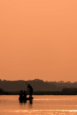 Erkekler bir nehir siluet günbatımı ışığı ile bir teknede