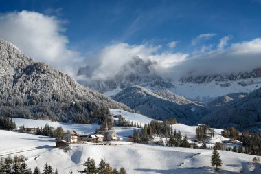 The church in the small village of St. Magdalena under a layer of fresh snow with in the background the Geisler group Dolomites mountain peaks in winter in the Villnoess valley in Trentino-Alto Adige, South Tyrol, Italy. clipart