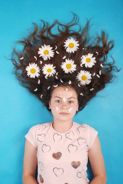 Studio mavi arka plan, yerde yatan saçlarını papatya ile genç bir kız portresi