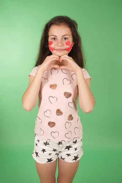 一个年轻女孩的肖像与心脏的象征在脸上 在绿色背景上隔离 — 图库照片