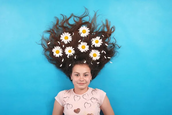 Portrait of a young girl with daisies in their hair lying on the floor, on blue background in studio