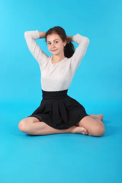 スタジオに青色の背景に対して床に座っている若い女の子 — ストック写真