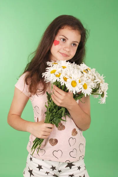 一个年轻女孩的肖像与一束 Chamomiles 和心脏的象征脸上 在绿色背景上隔离 — 图库照片